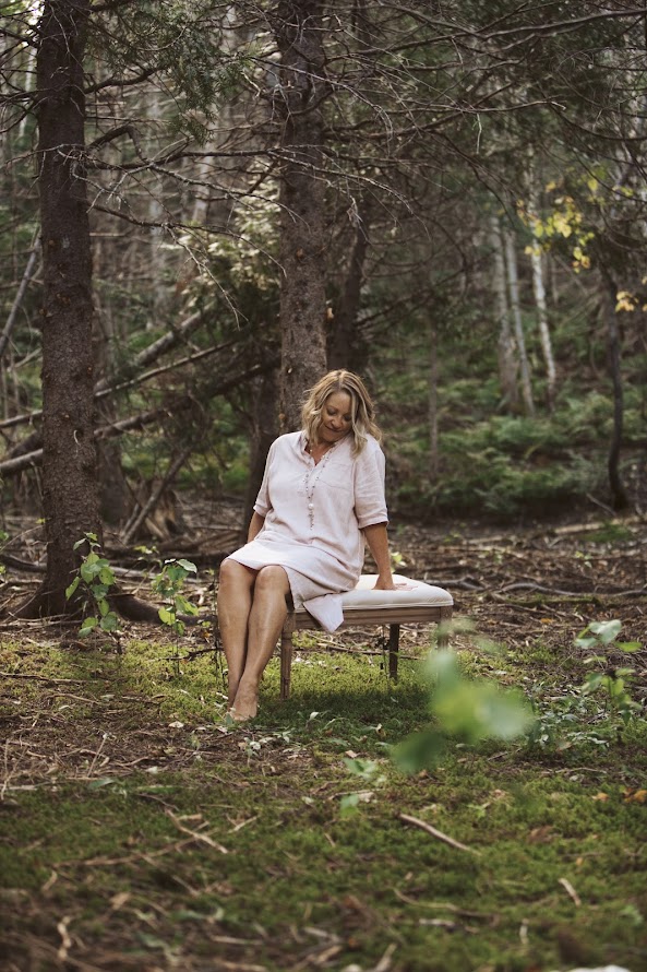Une femme habillée de blanc est assise sur un banc au milieu de la forêt gaspésienne
