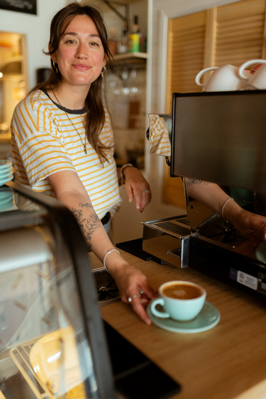 Une jeune femme souriante se tient derrière un comptoir. Elle sert un café fraîchement fait.