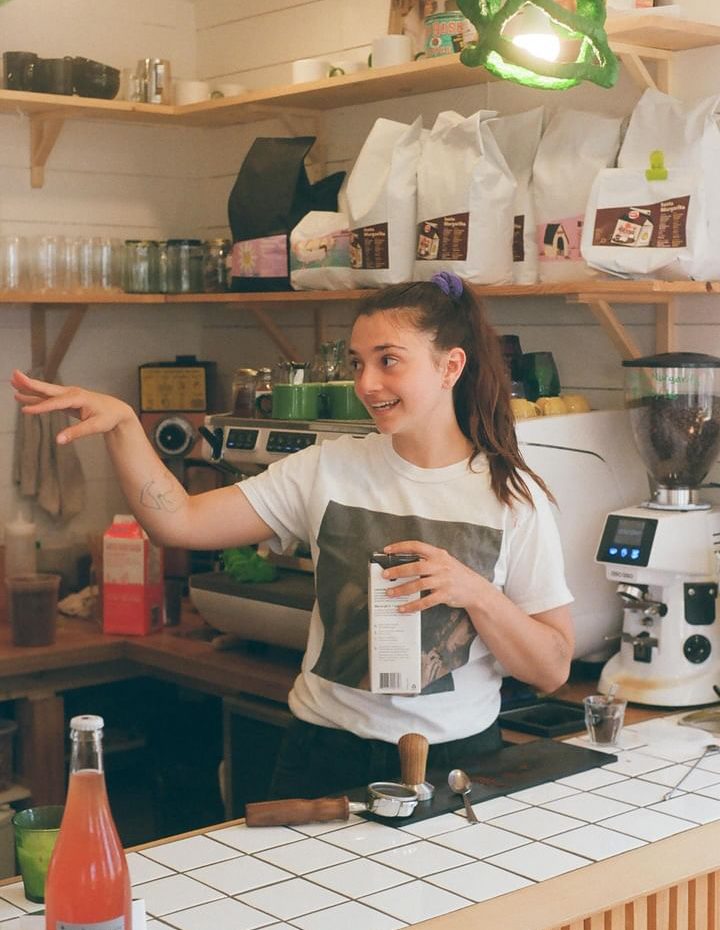 Une barista se tient derrière son comptoir et donne des indications